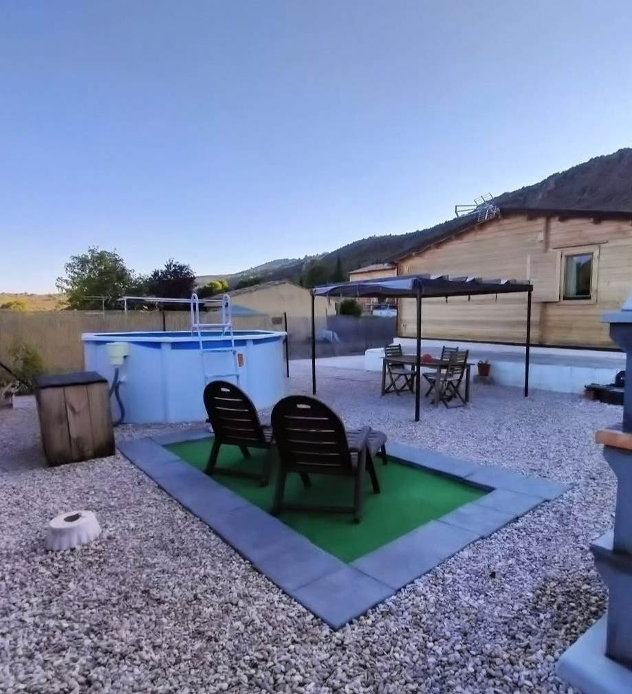 Patio trasero con piscina, zona de estar y vista a la montaña, en un día soleado.