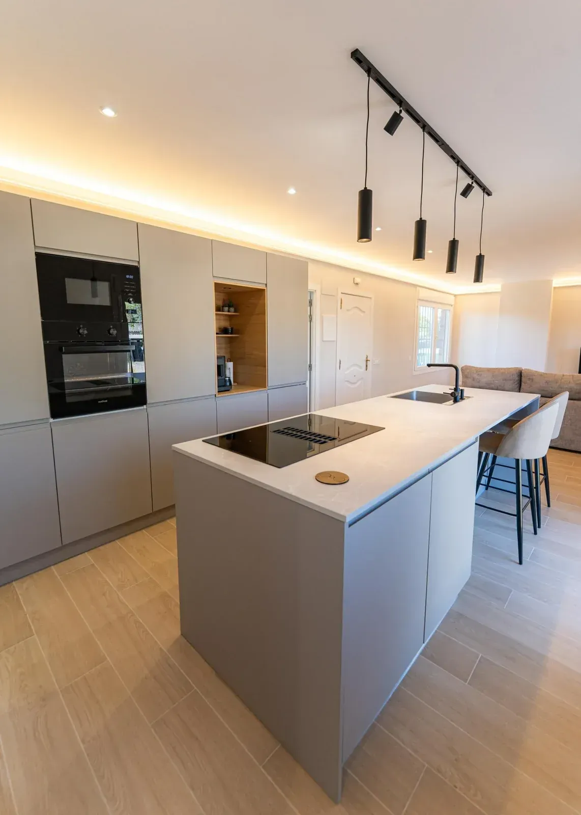 Cocina blanca moderna con isla, electrodomésticos integrados, lámparas colgantes y taburetes de bar