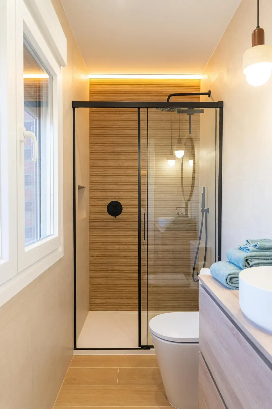 Baño moderno y estrecho con mampara de ducha de vidrio, paredes revestidas de azulejos con acabado de madera