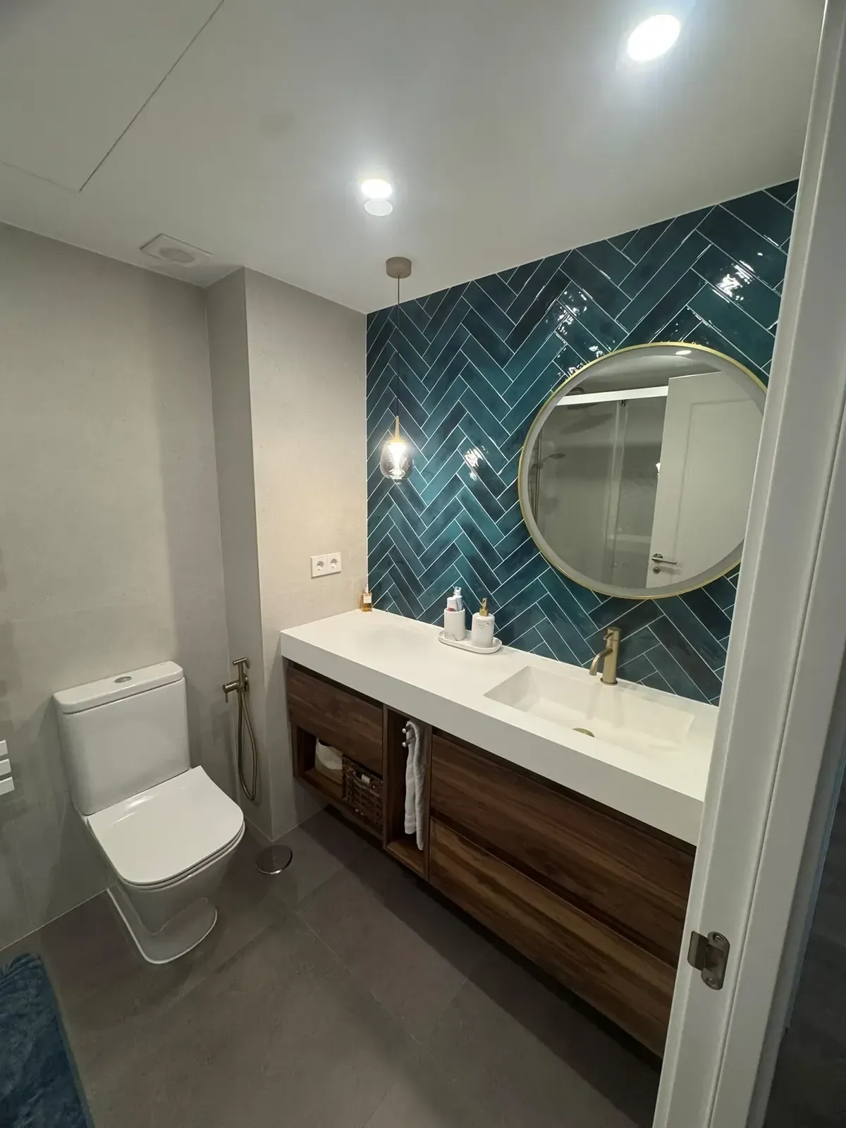 Baño moderno con inodoro, lavabo doble, espejo redondo y pared de acento geométrica en tonos verde azulado