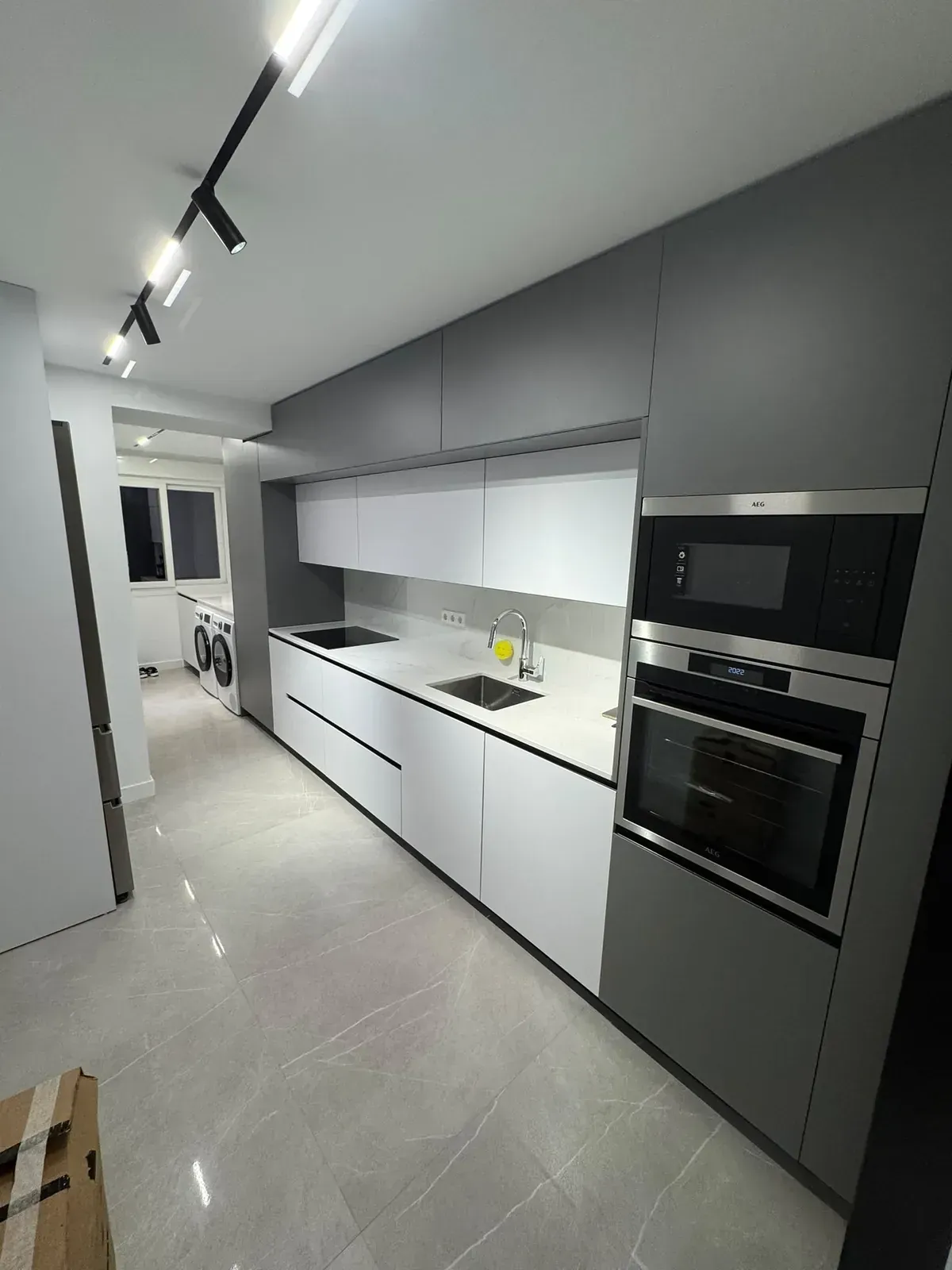 Cocina moderna en tonos grises con hornos integrados, armarios blancos y focos negros en rieles
