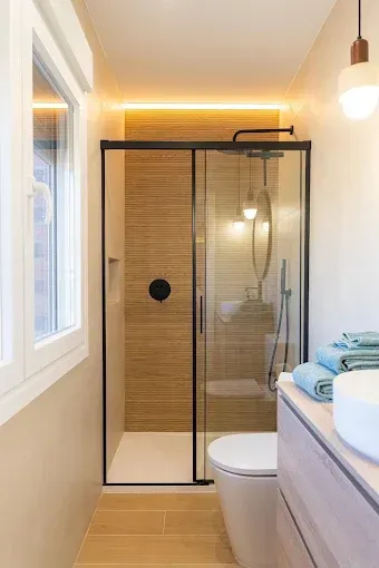 Baño moderno con ducha de cristal, detalles de azulejos con acabado de madera y un inodoro en primer plano