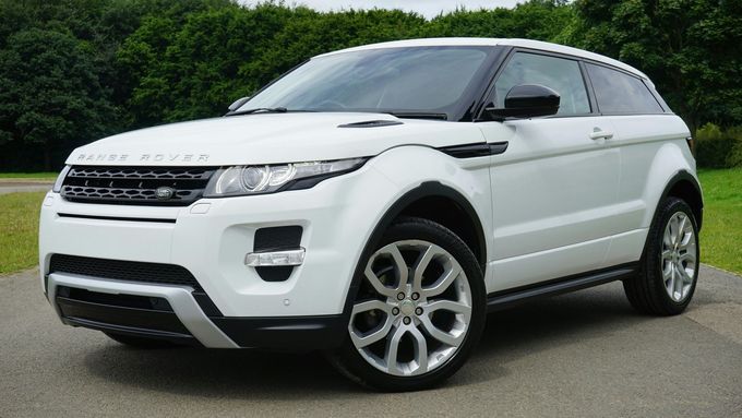 SUV Range Rover Evoque blanco estacionado en una carretera pavimentada, con césped y árboles al fondo.