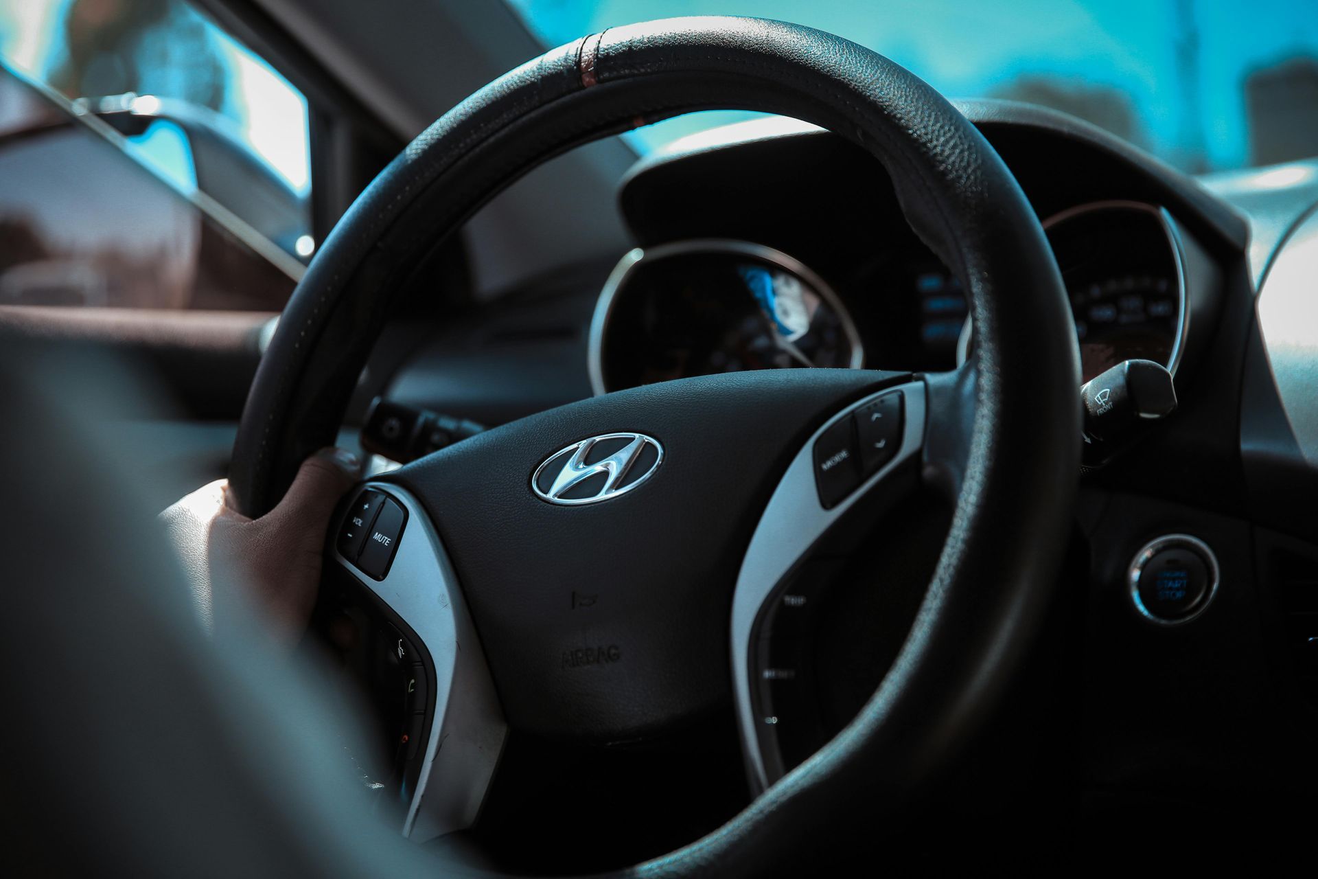 Mano de una persona en el volante de un automóvil Hyundai, vista interior, fondo azul.