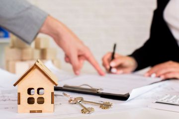 Maqueta de casa de madera, llaves y manos firmando un documento en un escritorio