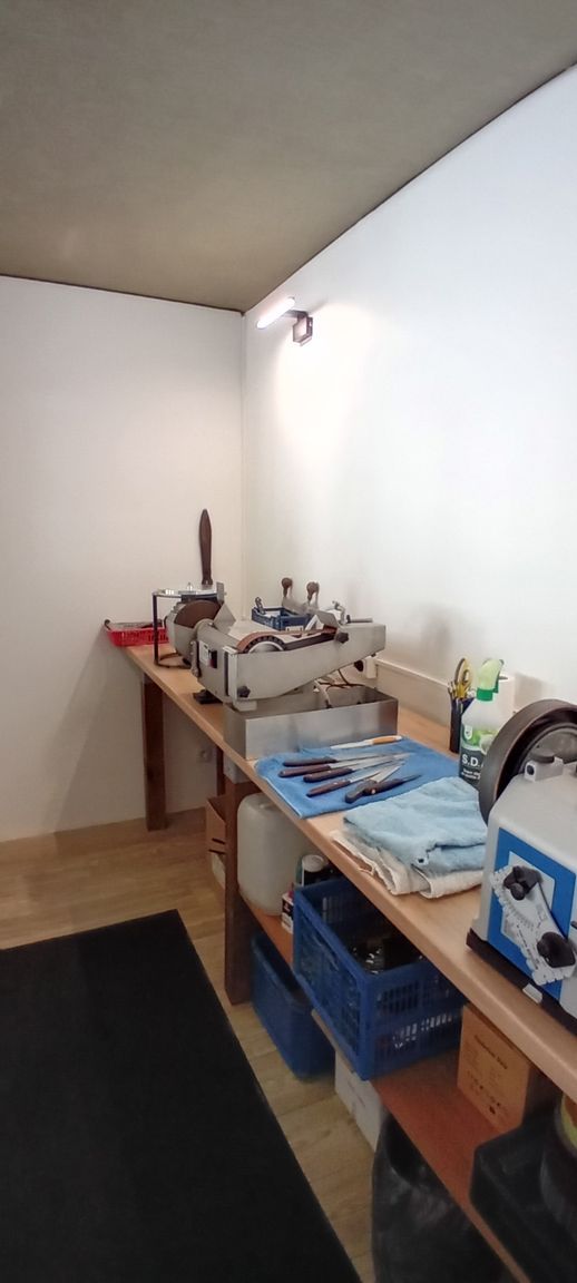 Un établi en bois, des outils, des bacs bleus et du matériel le long d’un mur blanc