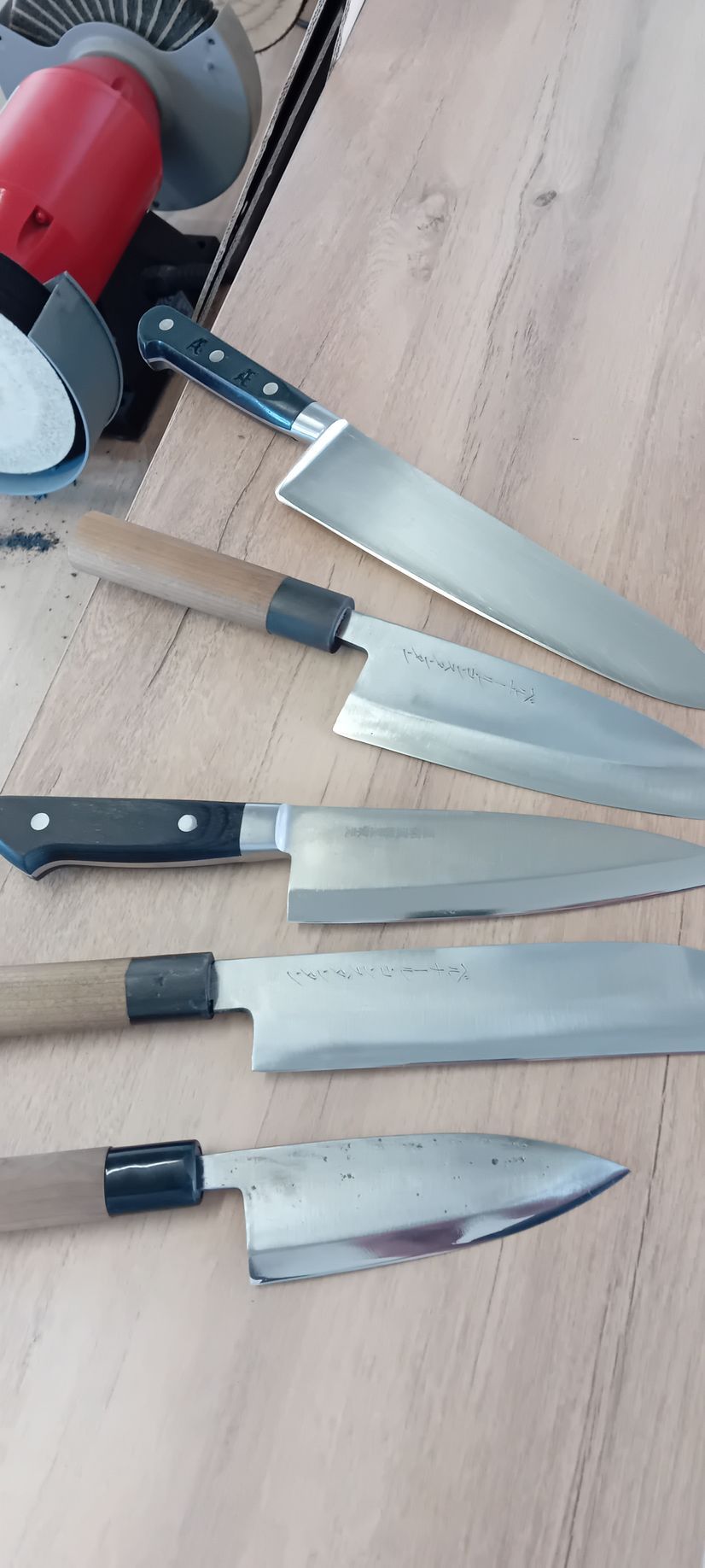 Cinq couteaux de cuisine à manche noir posés sur une table en bois.