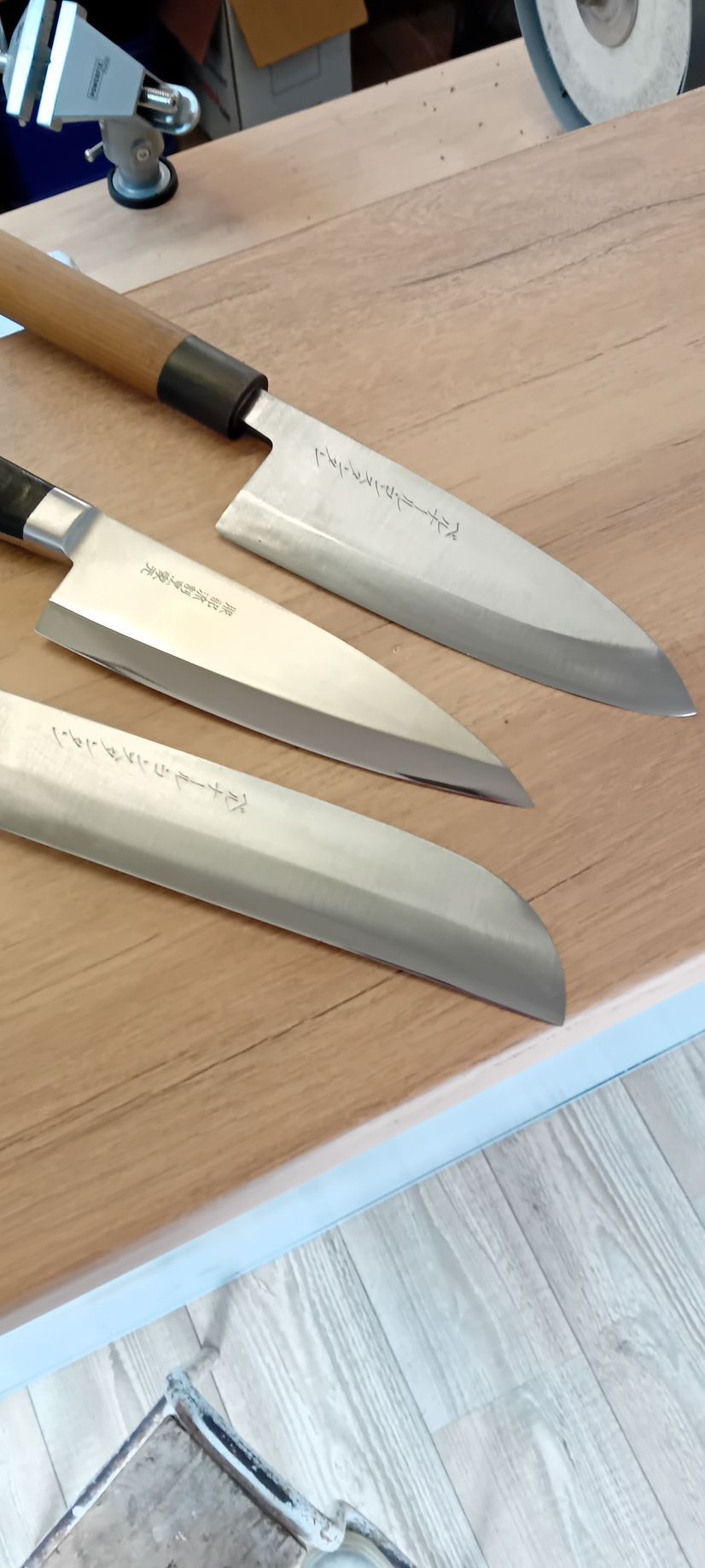 Trois couteaux de cuisine à manches noirs sur une planche à découper en bois.