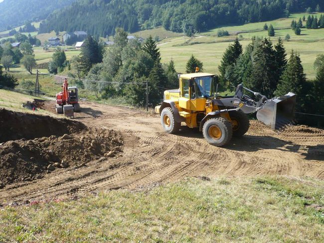 Deux engins de chantier nivelant un chemin de terre dans un paysage de colline verdoyante