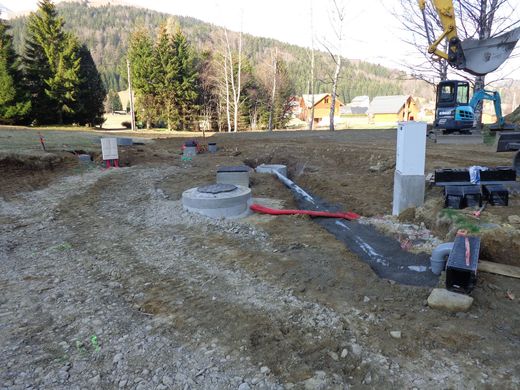 Chantier de construction extérieur avec tranchée, canalisations et équipements à proximité d'arbres et de collines.