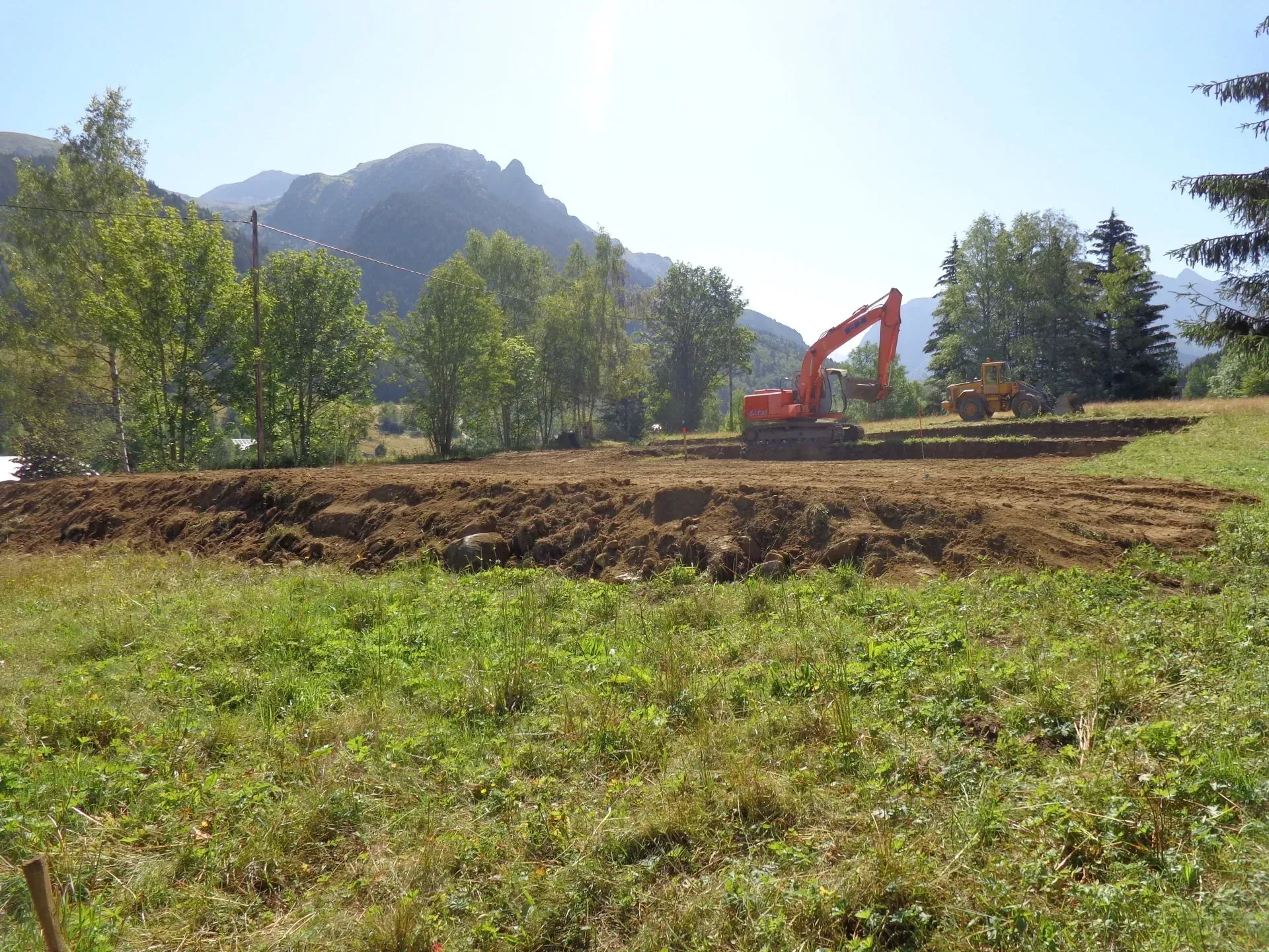 Engin de chantier sur un terrain en cours de travaux avec une montagne en fond