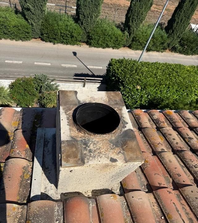 Conduit de cheminée sur toit en tuiles usées donnant sur une rue et de la verdure en contrebas