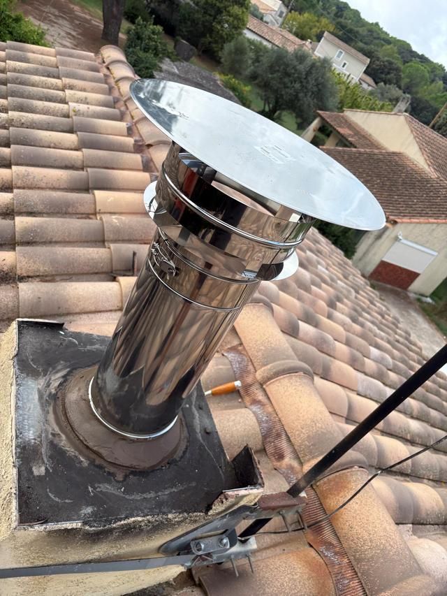 Cheminée de toit avec conduit et chapeau en métal brillant sur un toit de tuiles, avec des outils à proximité