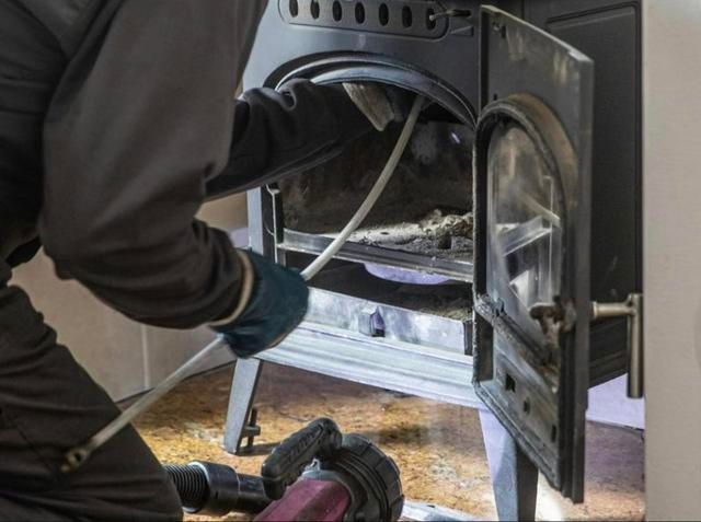 Personne nettoyant un poêle à bois, portant des gants et travaillant à l'intérieur de la porte ouverte