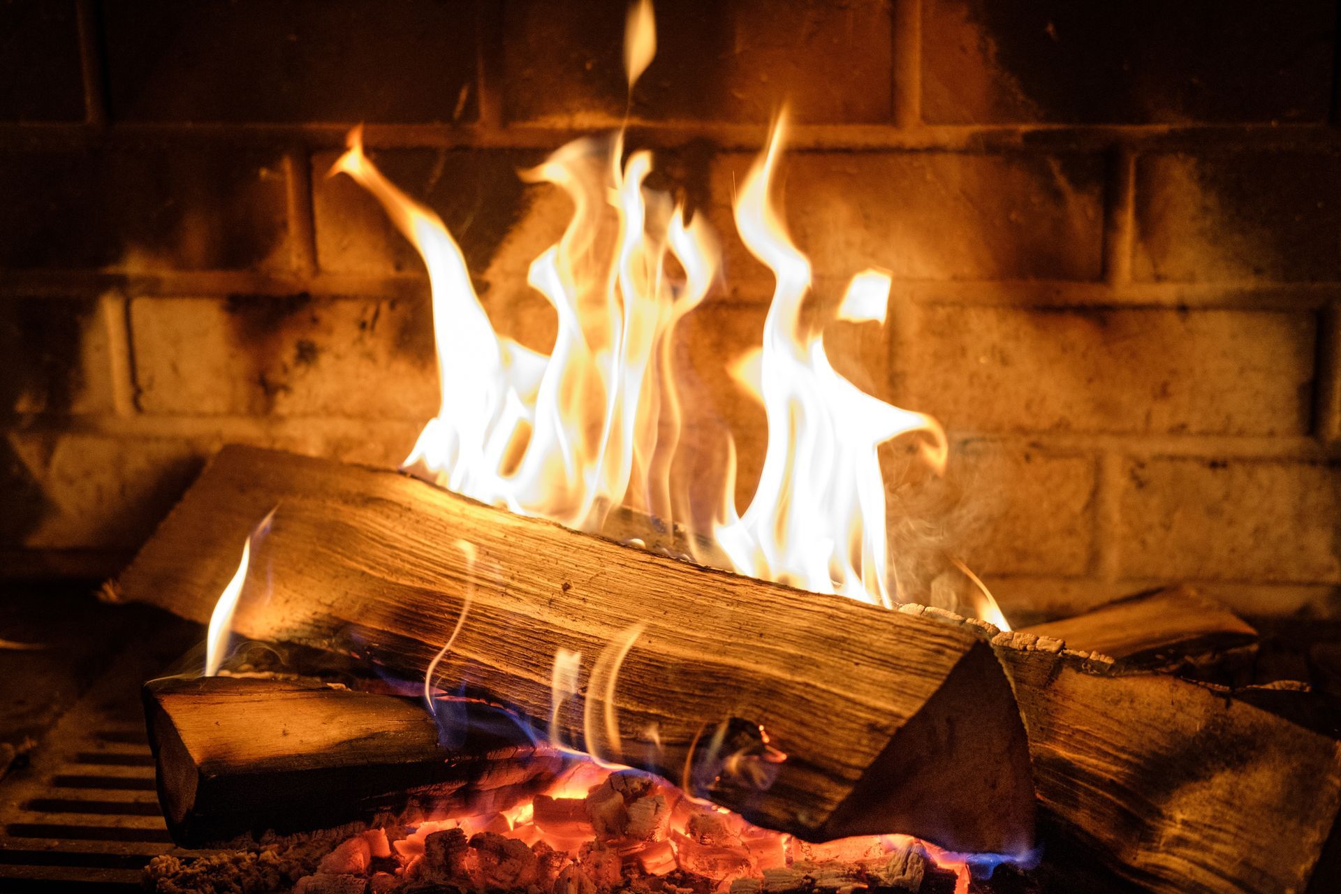 Des bûches incandescentes brûlent dans une cheminée en briques, les flammes d'un orange vif.