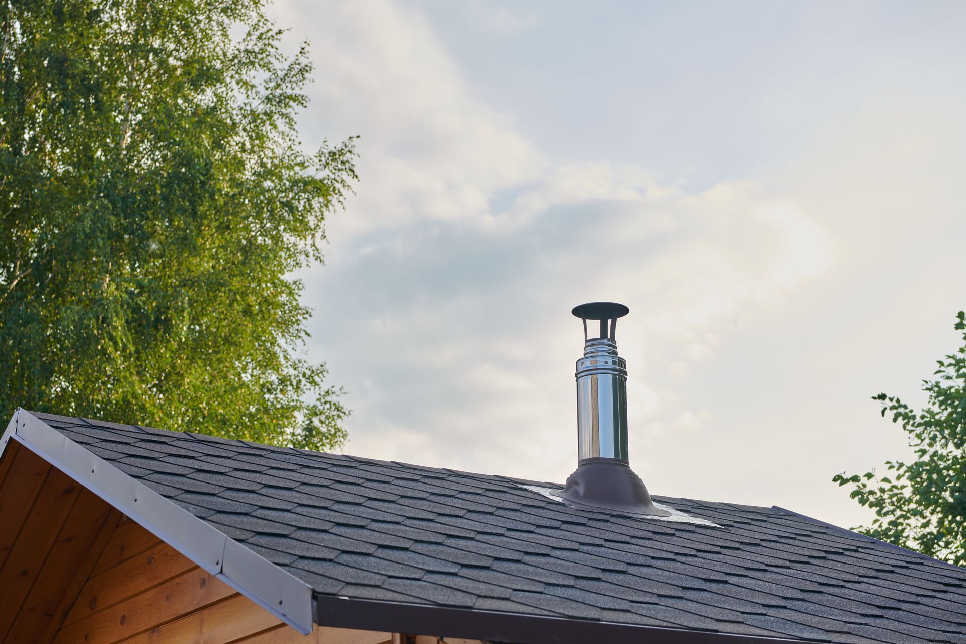 Toit de maison avec une cheminée métallique se détachant sur un ciel nuageux