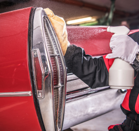 Un homme nettoie une voiture rouge avec un vaporisateur et un chiffon.