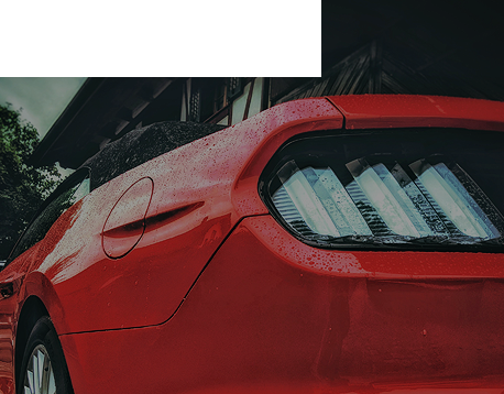 Une voiture rouge est garée devant un bâtiment sous la pluie.