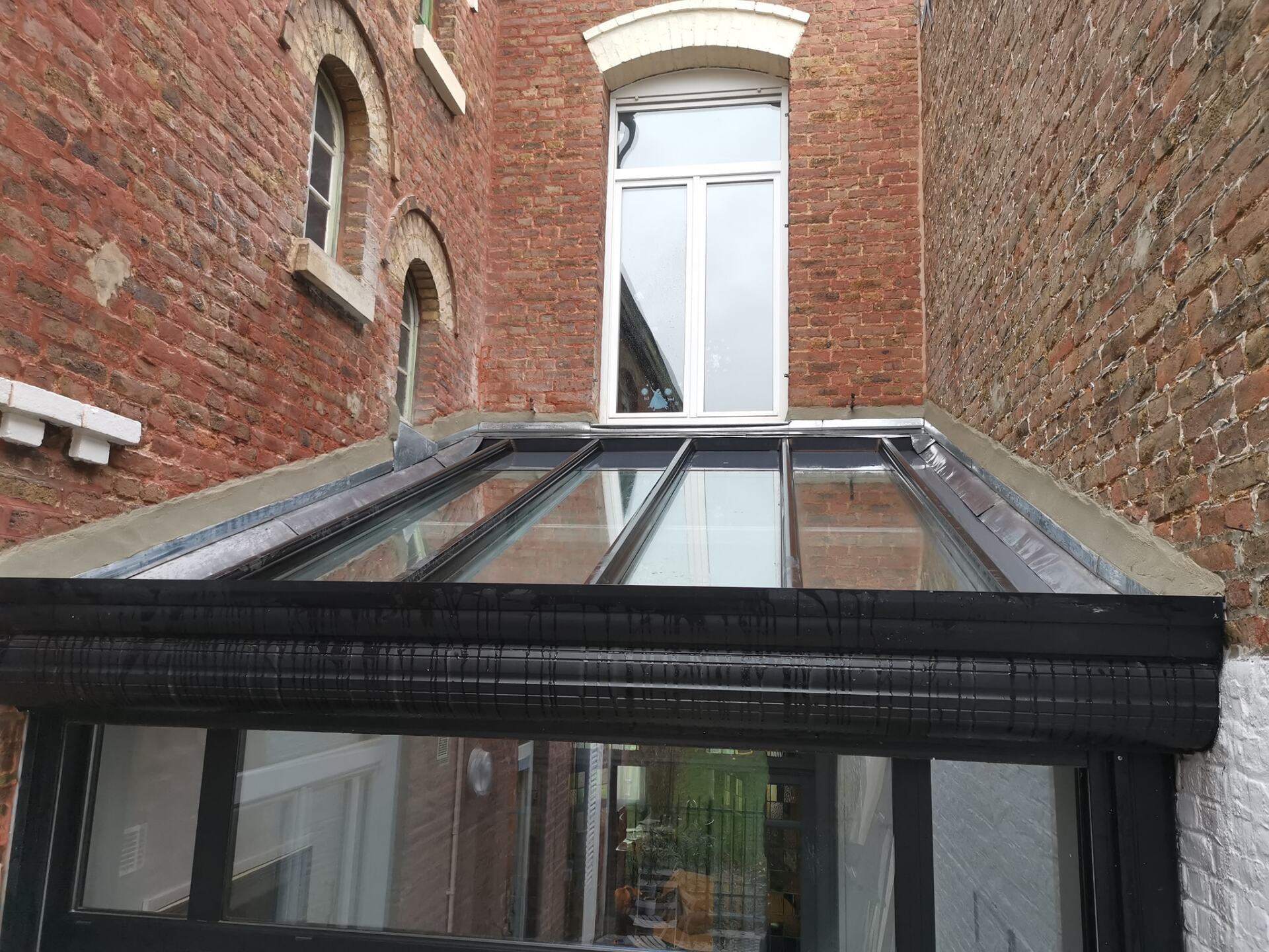 Véranda au toit de verre avec murs en briques et fenêtre au-dessus.