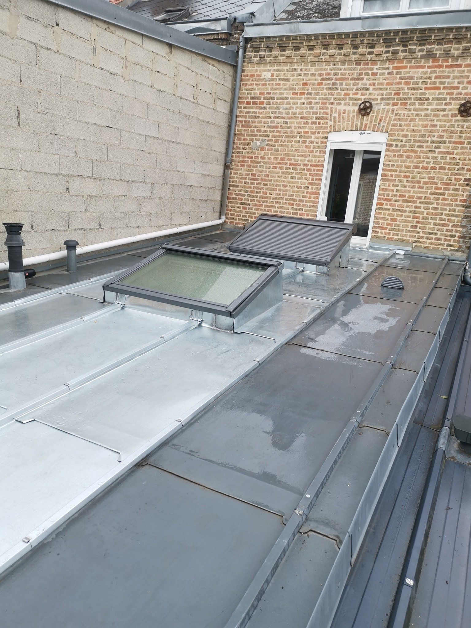 Toiture métallique avec puits de lumière et accès au toit. Mur de briques en arrière-plan.