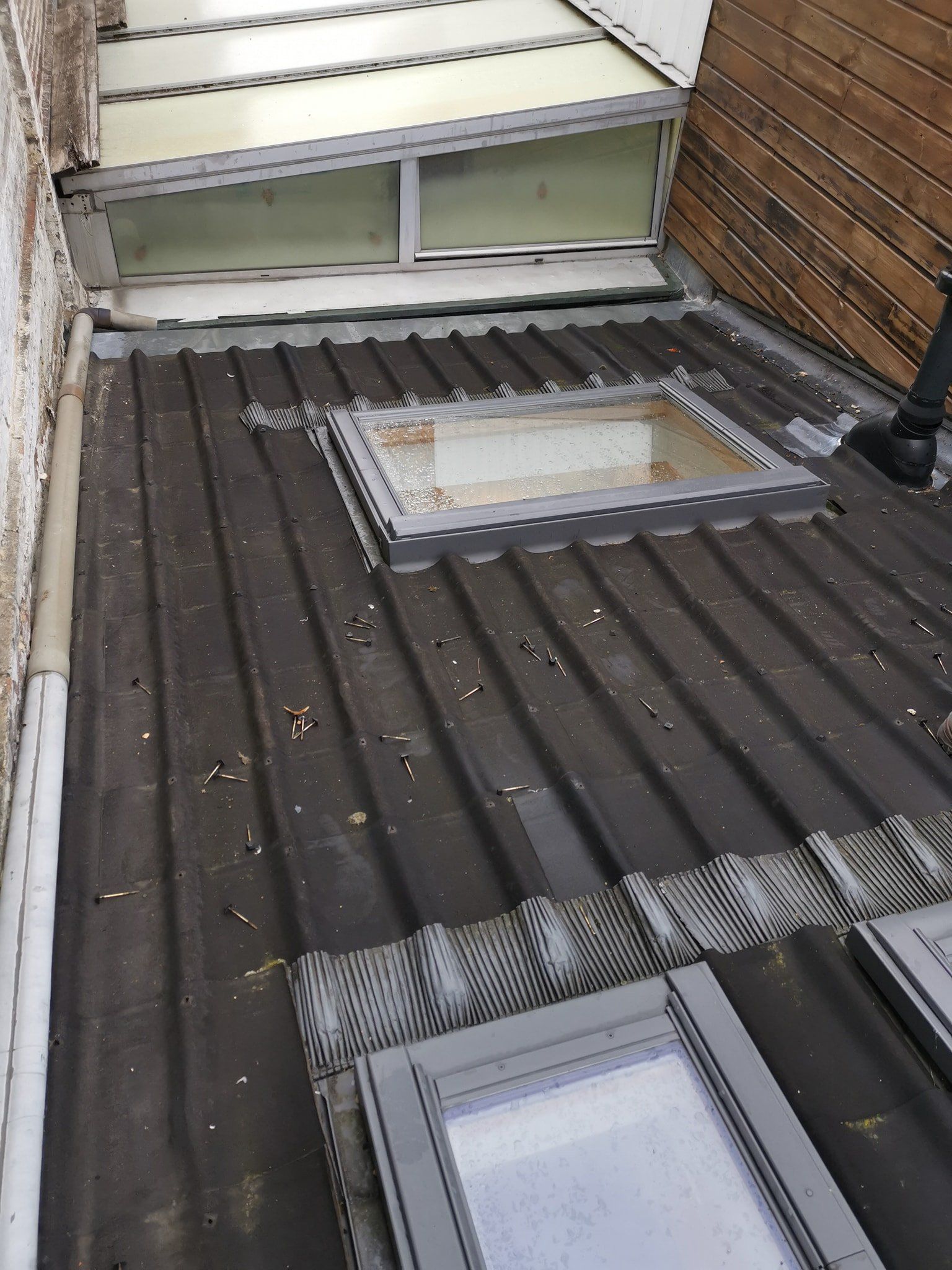 Toit ondulé foncé avec puits de lumière ; clôture en bois et murs blancs sont visibles.