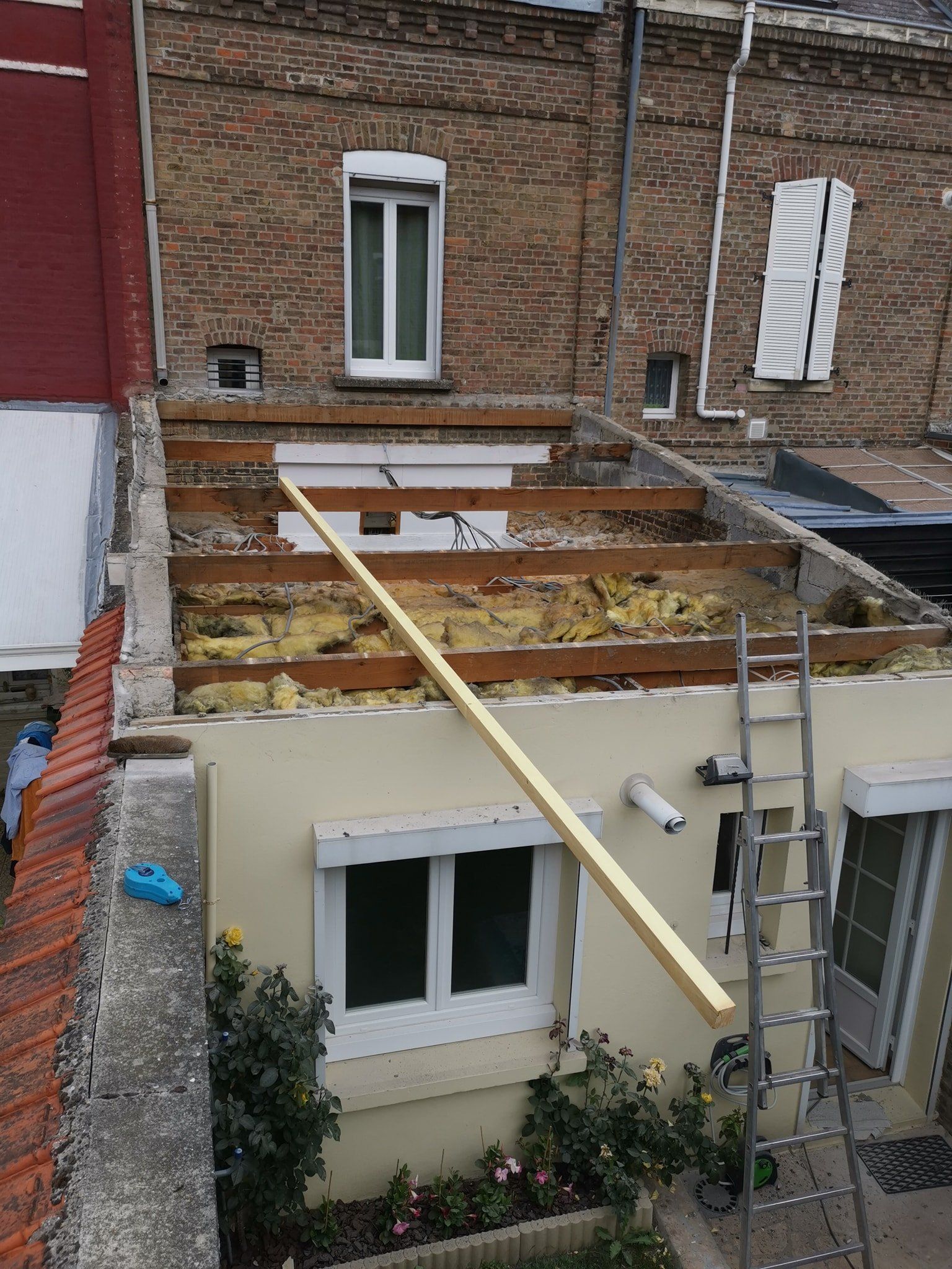 Toiture de maison en construction ; poutres en bois apparentes, isolation, échelle et une longue planche de bois.