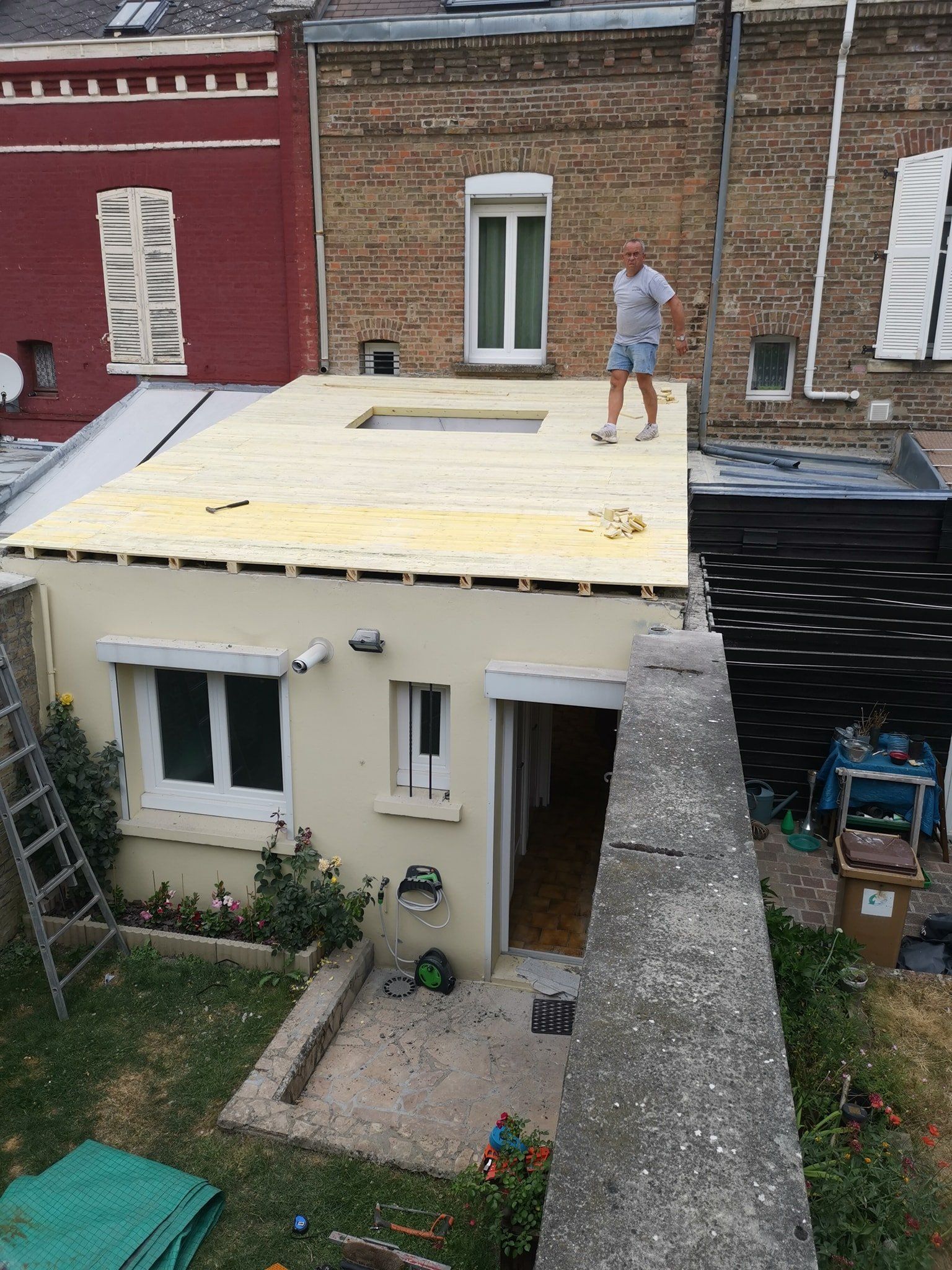 Ouvrier du bâtiment sur le toit, petite maison, cour, bâtiments en briques en arrière-plan.