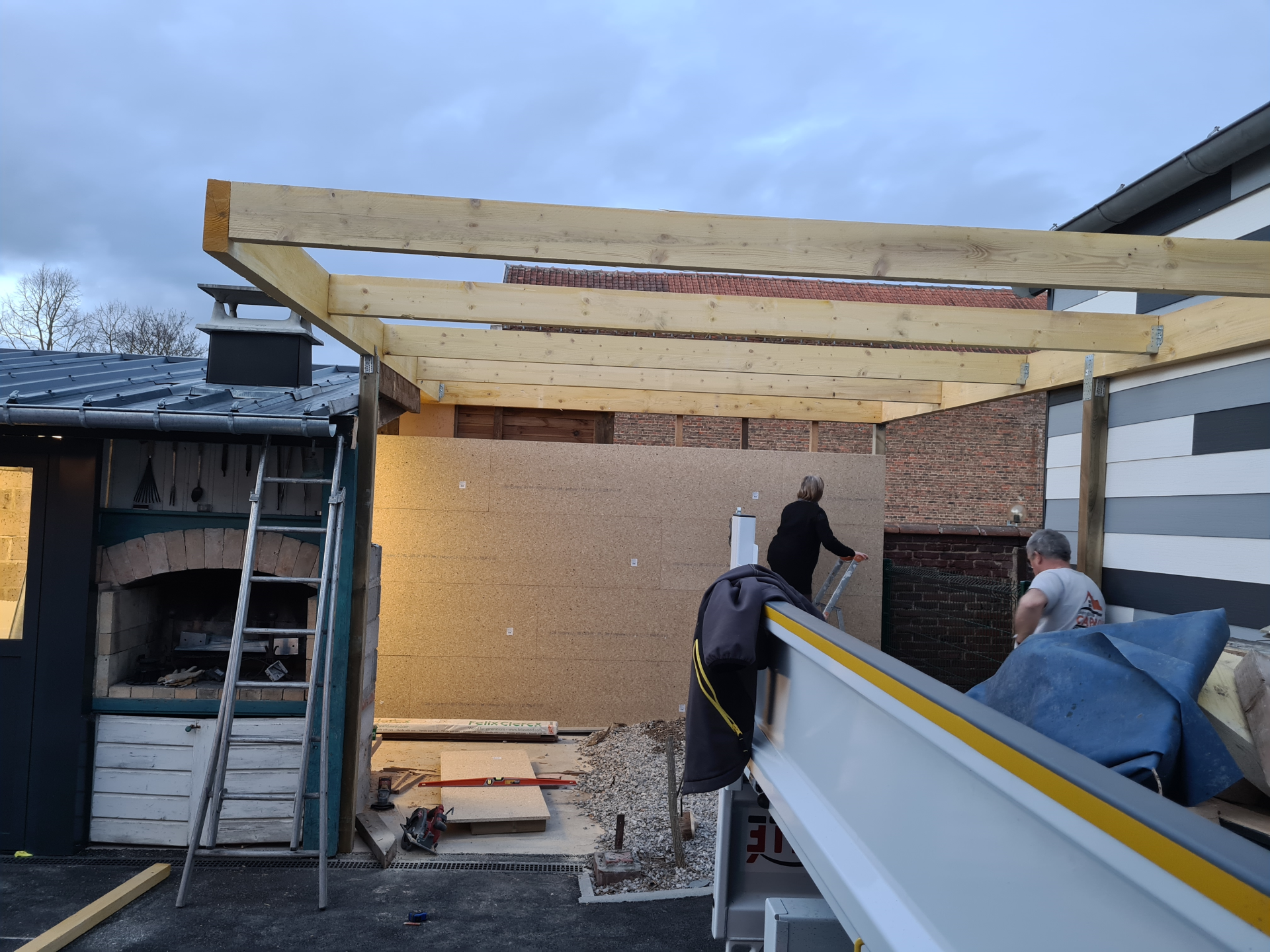 Chantier de construction : ouvriers construisant une structure de toit en bois, avec des briques et d'autres matériaux de construction visibles.