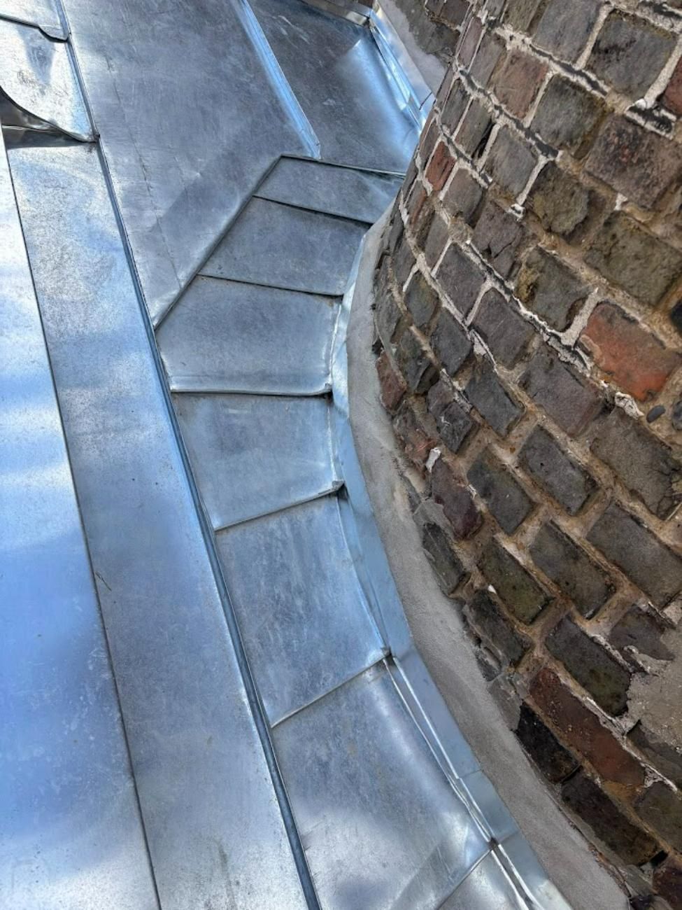 Gros plan d'un solin de toit en métal autour d'une cheminée en brique, avec des coutures détaillées.