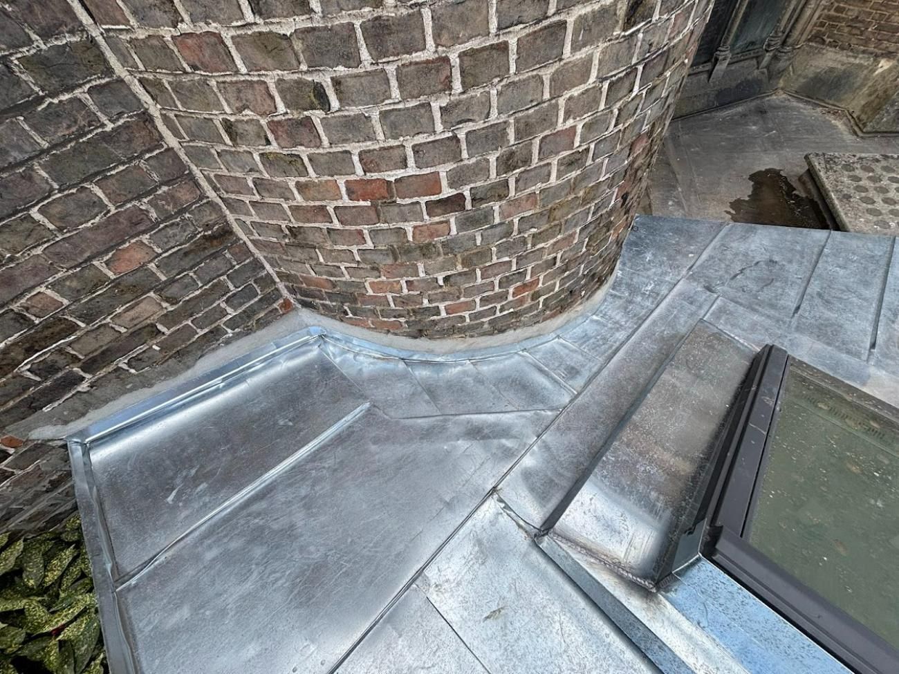 Toiture en plomb autour d'une structure en briques. Les feuilles de plomb argenté se courbent et rejoignent le mur de briques.