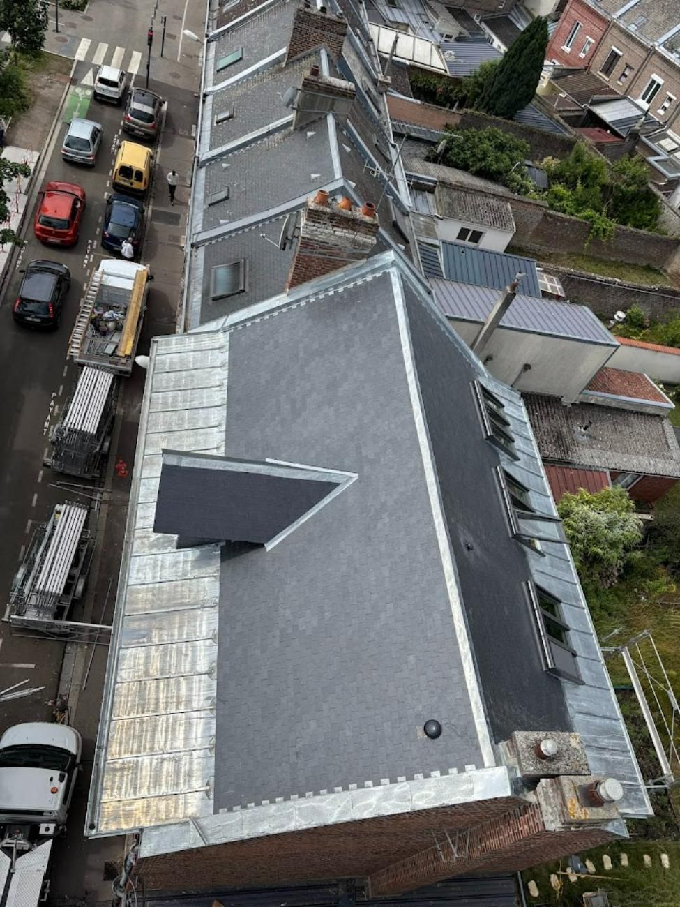 Vue des toits aux tuiles gris foncé inclinées à côté d'une rue avec des voitures garées.