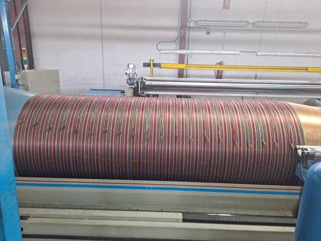 Un rollo grande de tela se está enrollando en una máquina en una fábrica.