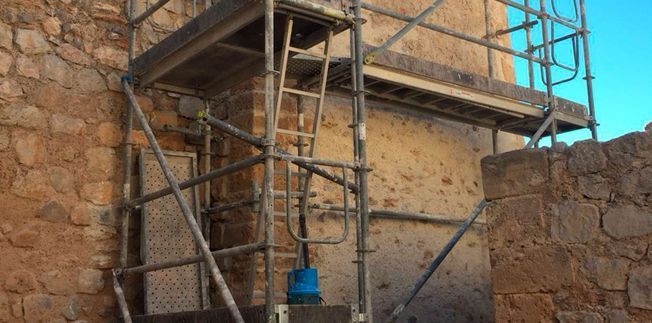 Andamio apoyado sobre un edificio de piedra, probablemente en construcción o reparación.