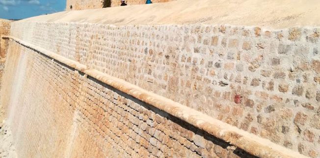Muros de piedra de una fortaleza en un día soleado, con un cielo azul al fondo.