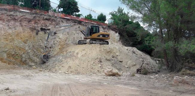 Una excavadora amarilla sobre un montículo de tierra está trabajando en una ladera, rodeada de árboles.