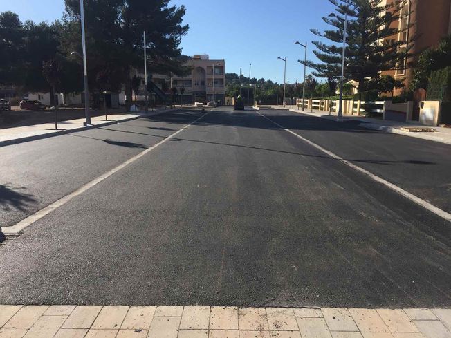 Carretera asfaltada recién pavimentada con marcas blancas, en una ciudad con edificios y árboles.