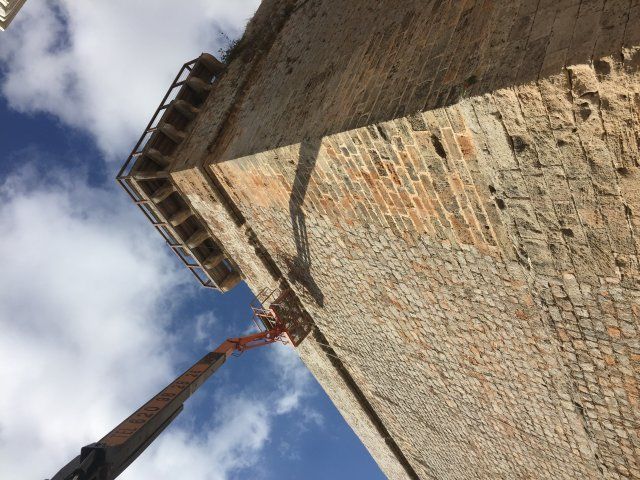 Una torre de ladrillo con un brazo elevador. El cielo está azul y nublado.