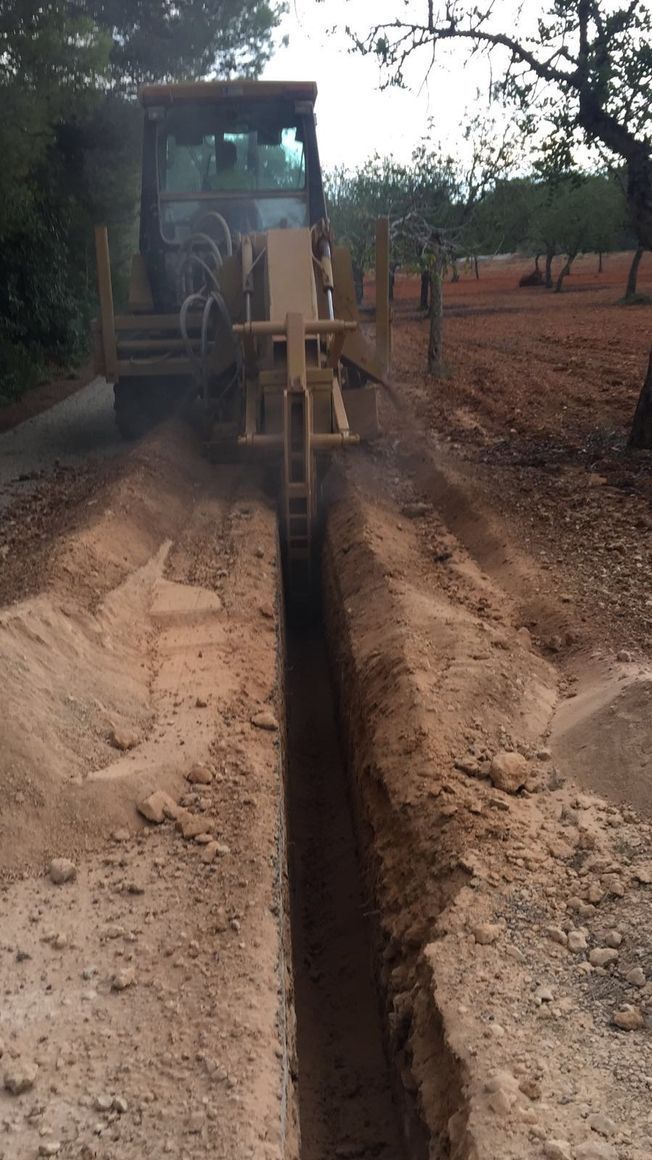 Una zanjadora cavando una zanja estrecha en tierra marrón, en un camino de tierra, en una zona rural.
