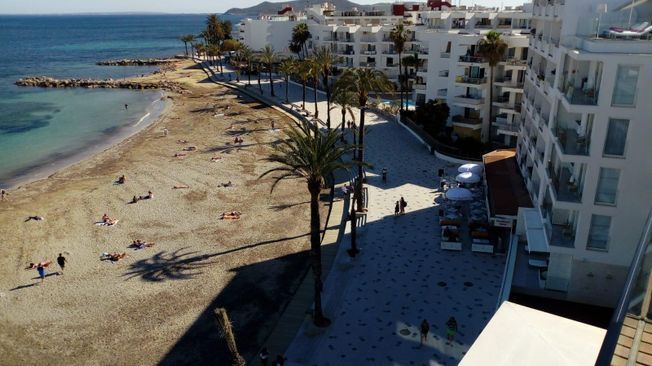 Playa con agua turquesa, palmeras y edificios a lo largo de la orilla.