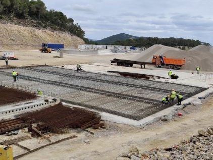 Obreros de la construcción con chalecos de seguridad ensamblan barras de refuerzo para cimientos de hormigón al aire libre.