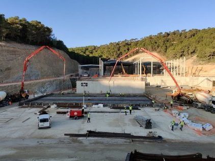 Obra con vertido de hormigón. Dos bombas de pluma rojas, trabajadores y una estructura parcialmente construida.