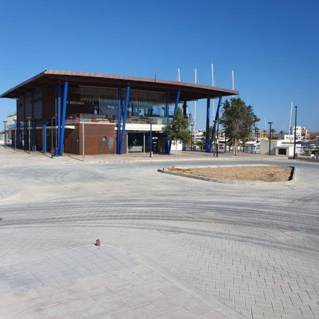 Edificio moderno con soportes azules, paredes de cristal y cubierta plana en zona pavimentada.