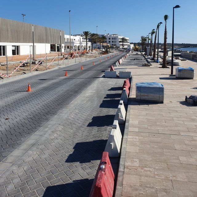 Construcción de carretera cerca del mar, con barreras, conos y un edificio parcialmente construido.