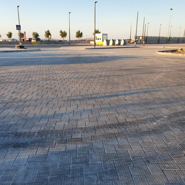 Estacionamiento pavimentado vacío con ladrillos grises estampados bajo un cielo azul.