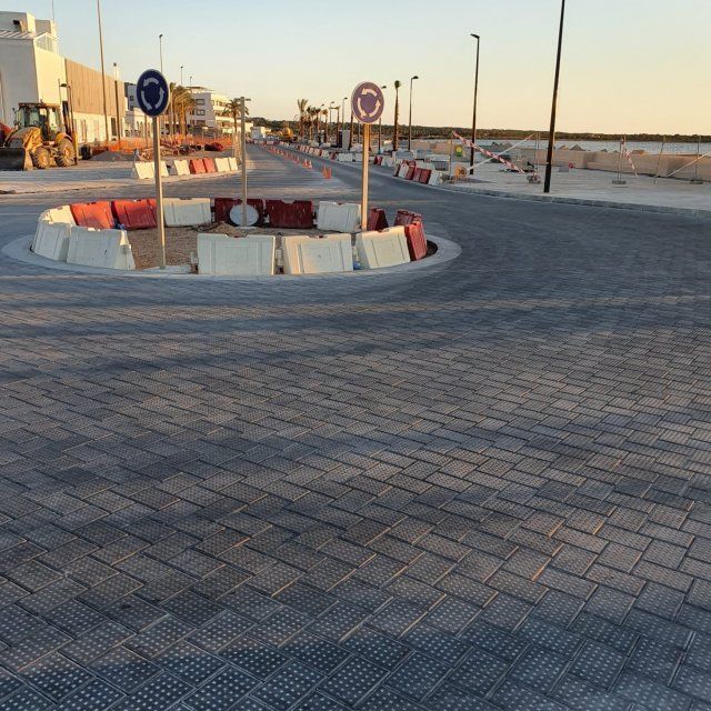 Una carretera asfaltada con una rotonda en construcción, marcada con señales y barreras de hormigón.