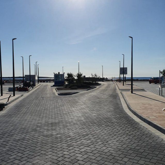 Camino pavimentado que se divide en dos, conduciendo a una zona de estacionamiento, bajo un cielo azul brillante.