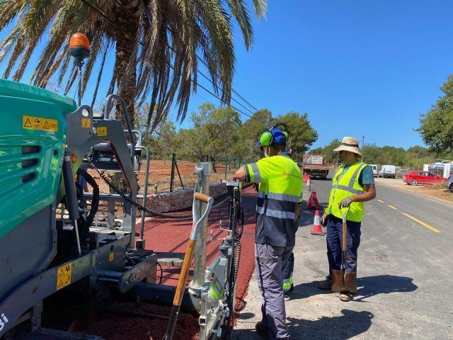 Los trabajadores de la carretera operan una máquina pavimentadora de asfalto en una carretera soleada.