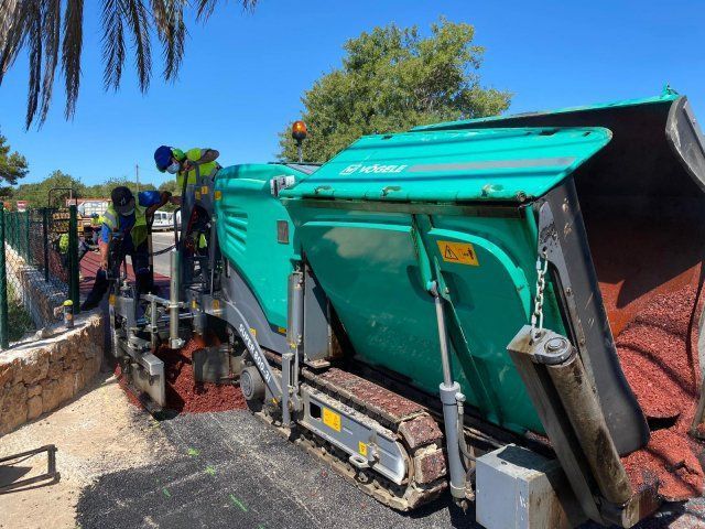 Máquina pavimentadora de asfalto colocando pavimento oscuro; trabajadores de la construcción cerca.