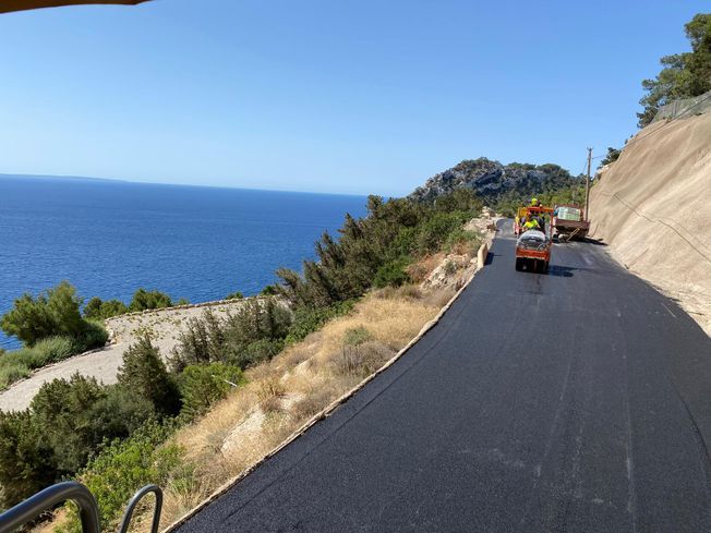 Obras en una pintoresca carretera costera. Una pavimentadora trabaja con el océano y el cielo de fondo.