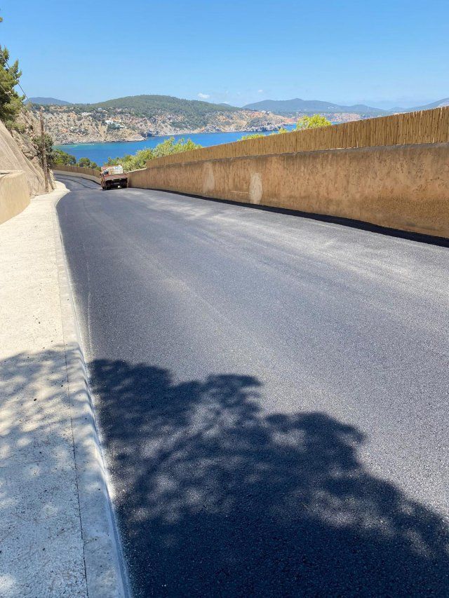 Carretera recién pavimentada que desciende hacia una vista costera; hay un vehículo circulando.